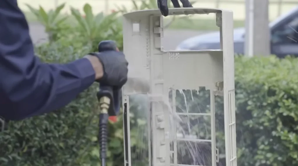 Technician spray cleaning the coil of an opened outdoor AC unit